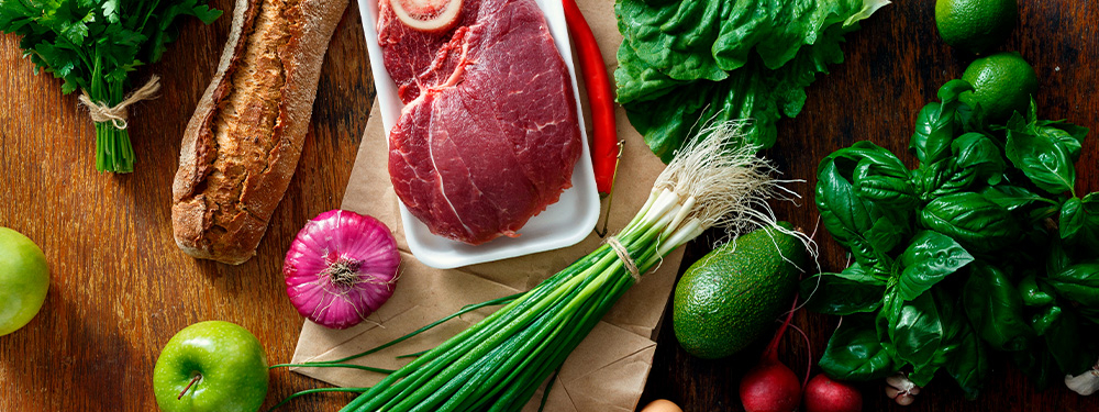 Bio-Gemüse, Bio-Fleisch, Bio-Kräuter und Bio-Brot nebeneinander auf einem Tisch.