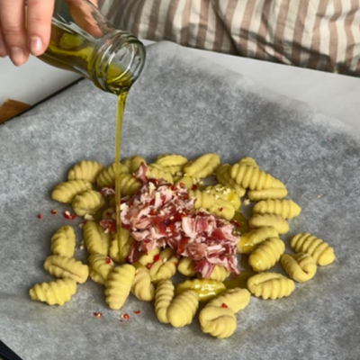 Bio-Gnocchi und Bio-Bauchspeck mit Bio-Olivenöl auf einem Blech vermengen.