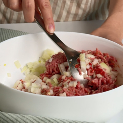 Bio-Weidejungrund Faschiertes wird mit Bio-Zwiebeln und Bio-Gewürzen in einer Schüssel vermengt.