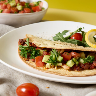 Bio-Lahmacun serviert auf einem Teller und daneben frische Bio-Zitrone und Bio-Tomaten.