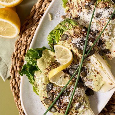 Die mit dem Bio-Caesar Dressing belegten Salatherzen serviert auf einem Teller und garniert mit frischer Bio-Zitrone, Parmesan und etwas Bio-Dill.