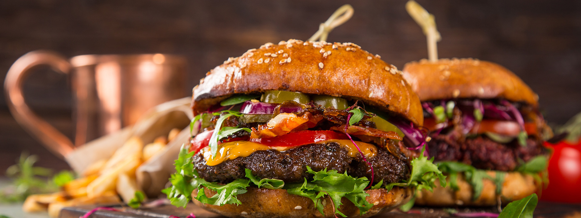 Frisch zubereitete Burger mir Bio-Fleisch Patty serviert auf einem Holzbrett und mit frischen Bio-Zutaten belegt.
