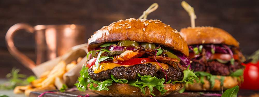 Frisch zubereitete Burger mir Bio-Fleisch Patty serviert auf einem Holzbrett und mit frischen Bio-Zutaten belegt.