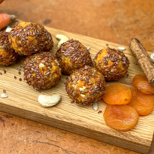 Leinsaat-Karotten-Marillen-Energy Balls auf einem Holzbrett, daneben Bio-Nüsse und Bio-Marillen.