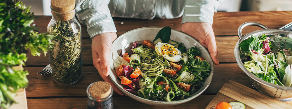 Bunte Healthy Bowl mit frischem Bio-Gemüse und Bio-Kernen sowie Bio-Samen, wird in den Händen einer Person gehalten.