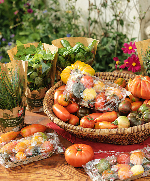 Verpackte Paradeiserräritäten in einer Schale mit Kräutern und losen Tomaten
