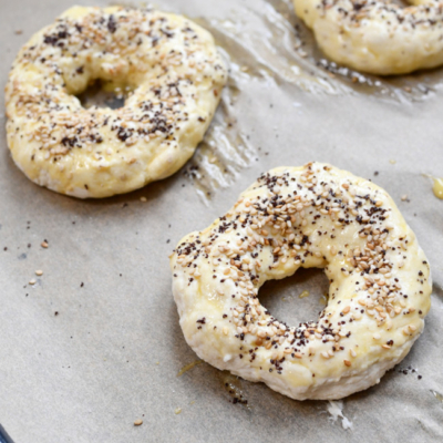 Die geformten und bestreuten Protein Bagels liegen auf einem Backblech.