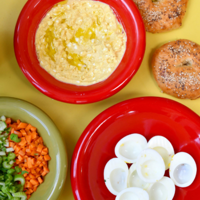 Bio-Eier, Bio-Cottage Cheese, Bio-Senf und Curry sind in einer Schüssel miteinander verrührt, daneben ist gehakter Bio-Sellerie und Bio-Karotten in einer Schüssel.