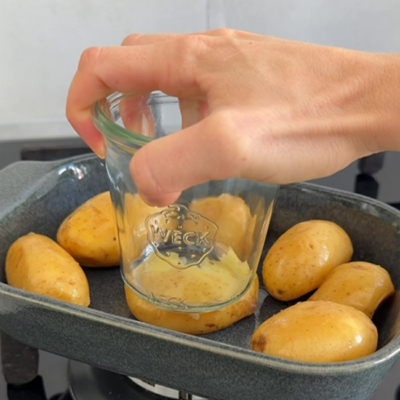 Die vorgegarten Bio-Mini-Erdäpfel werden in mit einem Glas flach gedrückt.