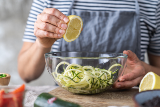 Jemand drückt eine Bio-Zitrone über Zucchininudeln aus.