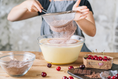Jemand siebt ein Mehlgemisch in die Bio-Eiermasse.