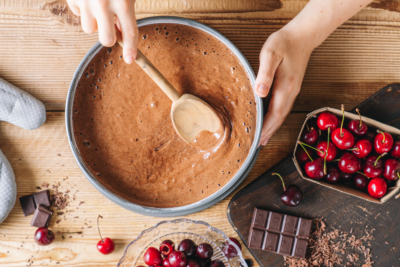 Jemand verstreicht einen Teig in einer Kuchenform, daneben steht eine Schüssel mit Bio-Kirschen.