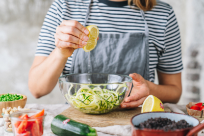Jemand presst Bio-Zitronensaft in eine Schüssel mit Zucchininudeln.