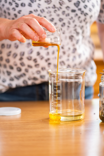 Eine Person schüttet einen Ölauszug in einen Glas-Messbecher mit Bienenwachs.