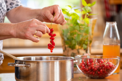 Jemand zupft Bio-Ribisel und gibt sie in einen Topf.