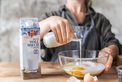 Jemand schüttet Ja! Natürlich Bio-Vollmilch in eine Schüssel mit Ei und Mehl.