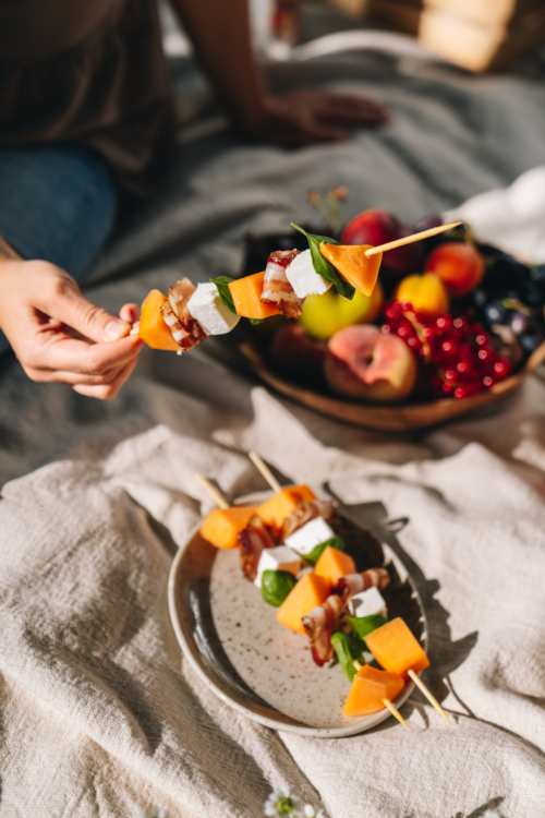 Jemand hält einen Spieß mit Bio-Früchten, Speck und Käse.