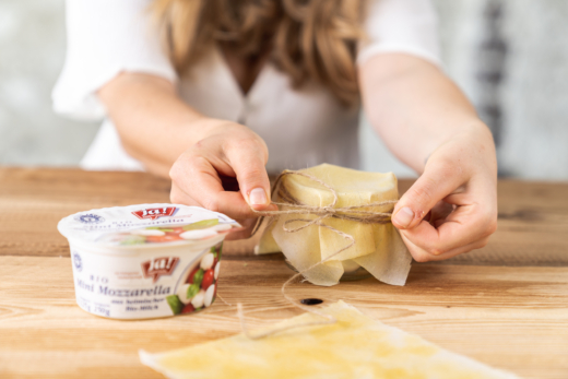 Jemand deckt ein Glas mit Ja! Natürlich Bio-Mini-Mozzarella mit einem Bienenwachstuch ab.