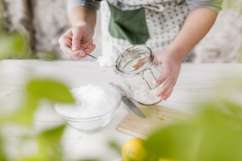 Jemand gibt Meersalz von einem Glas in eine Schüssel.
