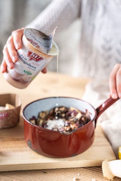 Jemand gießt Ja! Natürlich Bio-Schlagobers über Champignons in einem Topf.