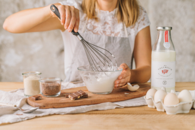 Jemand schlägt Eiweiß steif, daneben eine Flasche Ja! Natürlich Bio-Vollmilch.