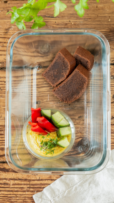 Eine Glasschale mit Gemüsesticks in Bio-Hummus und drei Stück Schoko-Bananenbrot.
