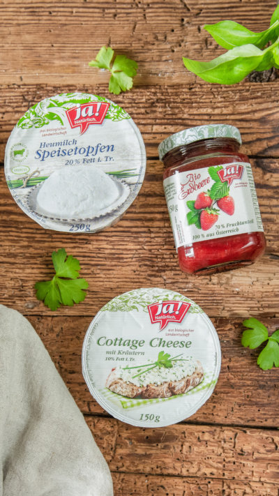 Eine Packung Ja! Natürlich Bio-Speisetopfen und Cottage Cheese neben einem Glas Erdbeermarmelade.