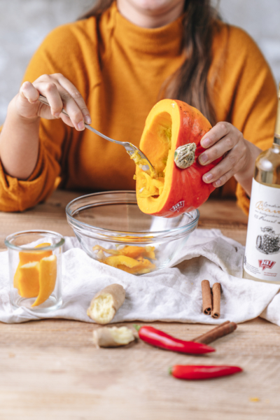 Jemand höhlt einen Kürbis aus. Daneben steht eine Flasche Ja! Natürlich Bio-Condimento Bianco.