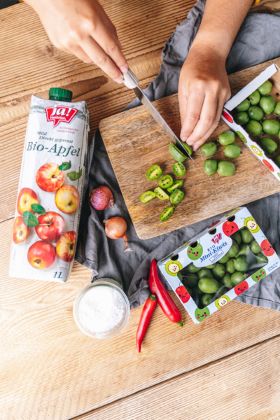 Jemand schneidet Ja! Natürlich Bio-Kiwis, daneben liegt eine Flasche Apfelsaft.