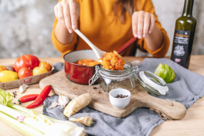 Jemand füllt Paradeiser-Stangensellerie-Chutney in ein Glas, daneben eine Flasche Ja! Natürlich Bio-Olivenöl.