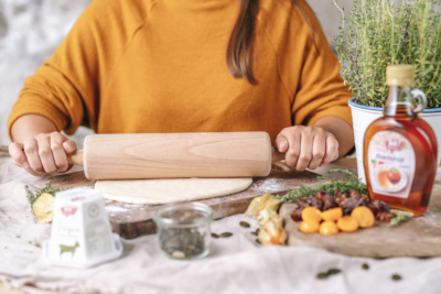 Jemand rollt Teig aus. Daneben stehen Ja! Natürlich Bio-Ahornsirup und Bio-Ziegenfrischkäse.