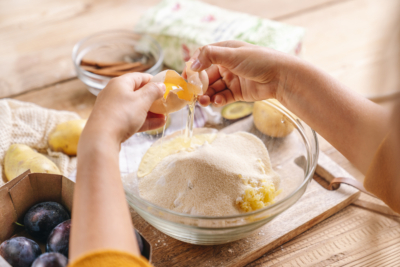 Jemand schlägt ein Ei über einer Schüssel mit Ja! Natürlich Bio-Weizenmehl auf.