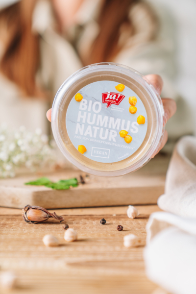 Jemand hält eine Packung Ja! Natürlich Bio-Hummus.