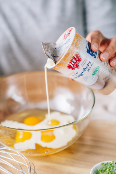 Jemand schüttet Ja! Natürlich Bio-Schlagobers in eine Schale mit aufgeschlagenen Eiern.