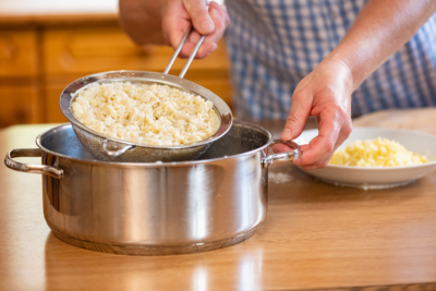 Jemand holt mit einem Sieb Nudeln aus kochendem Wasser.