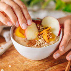Jemand taucht eine Apfelspalte in einen Bio-Porridge.
