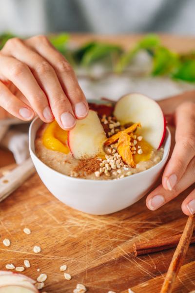 Jemand taucht eine Apfelspalte in einen Bio-Porridge.