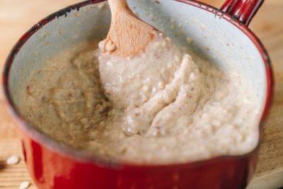 Jemand rührt Porridge in einem Topf um.