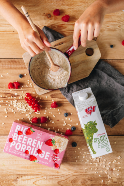Jemand bereitet einen Ja! Natürlich Bio-Beeren Porridge mit Heublumenmilch vor.