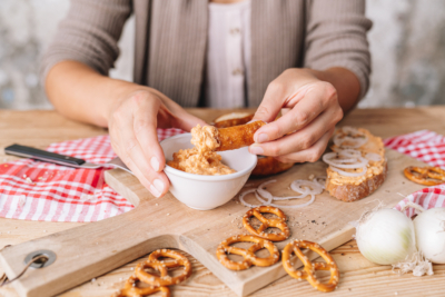 Jemand tunkt eine Brezel in einen Obatzter-Aufstrich.