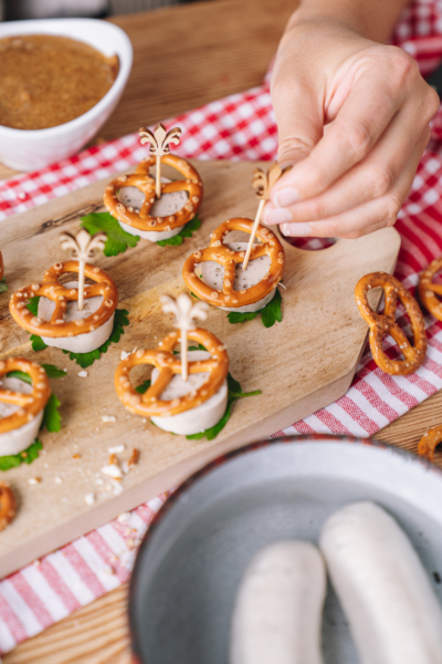 Jemand serviert in Scheiben geschnittene Weißwürste mit Mini-Brezn als Topping.