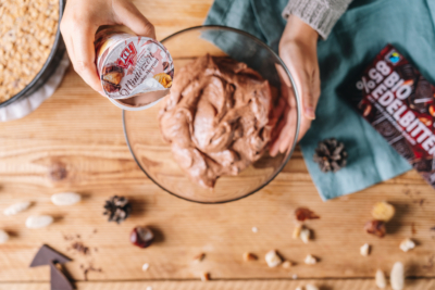 Jemand gibt einen Becher Ja! Natürlich Bio-Joghurt Winterzeit in eine Schüssel.