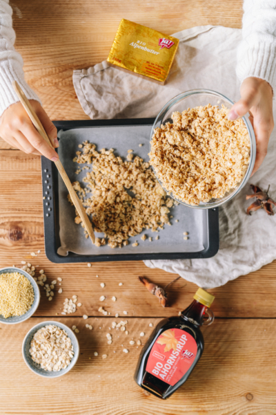 Jemand verteilt Bio-Hafercrumble auf einem Blech.