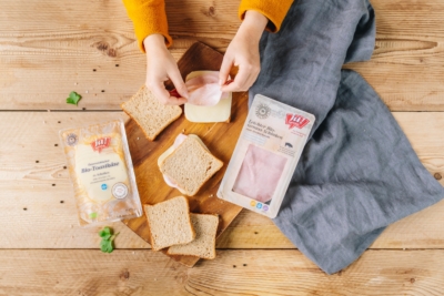 Jemand belegt Scheiben Brot mit Bio-Wurst und Käse von Ja! Natürlich.