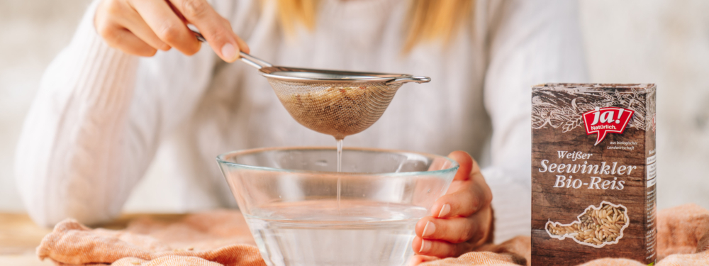 Jemand wäscht Ja! Natürlich Bio-Seewinkler Reis, eine Packung steht daneben.