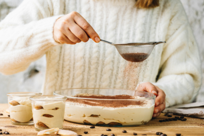 Jemand siebt Kakao auf ein Tiramisu.