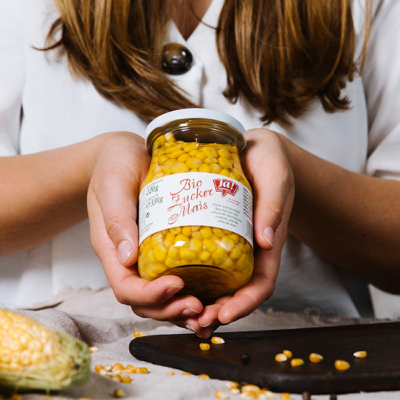 Jemand hält ein Glas Ja! Natürlich Bio-Goldmais.