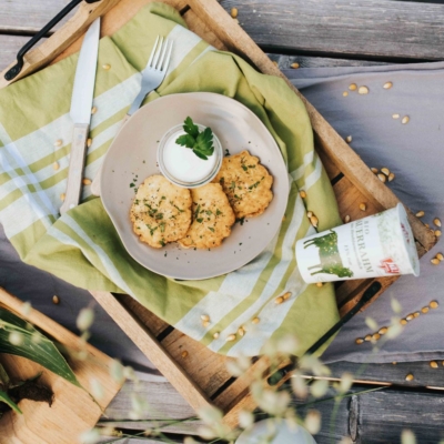 Ein Teller Mais-Laibchen mit einem Becher Ja! Natürlich Bio-Sauerrahm.