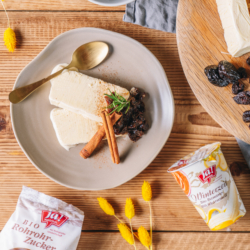 Banane-Milchkaramell-Joghurt-Parfait mit Pflaumensauce, daneben ein Becher Ja! Natürlich Bio-Winterzauber Joghurt.