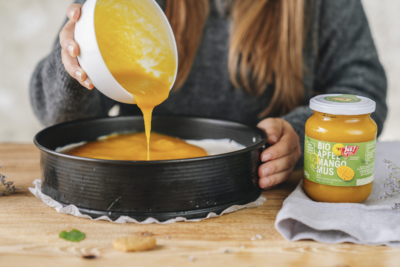 Jemand schüttet einen Fruchtspiegel aus Ja! Natürlich Bio-Apfel-Mango-Mus über eine Torte.